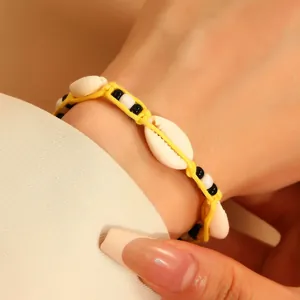 Detail of yellow braided Bohemian bracelet featuring natural white cowrie shells and beads