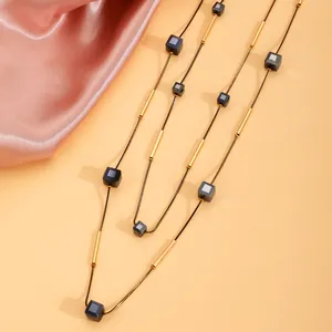 Detail einer minimalistischen langen Kette mit schwarzen Würfelperlen und Goldröhren