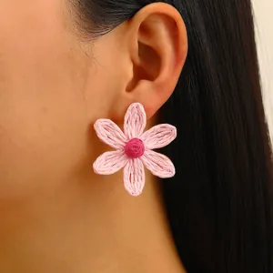 Pink woven raffia sunflower earring displayed on a model in a bohemian resort style