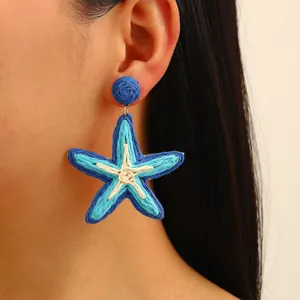 Star shaped woven raffia earrings in blue and white colors for a bohemian holiday look