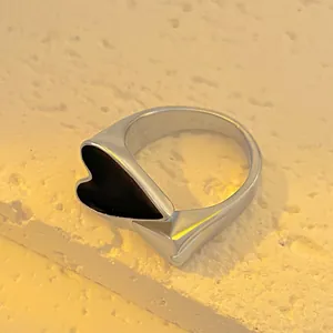 Minimalist silver ring with black heart design on natural stone textured background