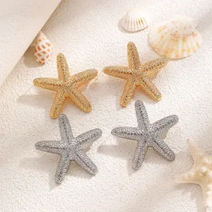 Detail of gold and silver starfish earrings on white sand with natural seashells
