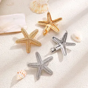Macro shot of gold and silver starfish earrings with hammer texture on white sand