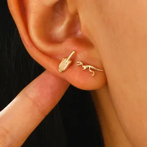 Detalle de pendientes dorados creativos con forma de dedo corazón y de un dinosaurio