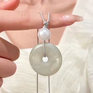 Dettaglio di un ciondolo con perla bianca e finta giada verde su cordino grigio