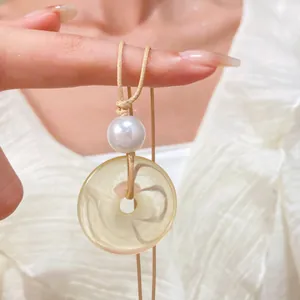 Dettaglio del ciondolo ad anello in finta giada con perla su collana in corda intrecciata indossata