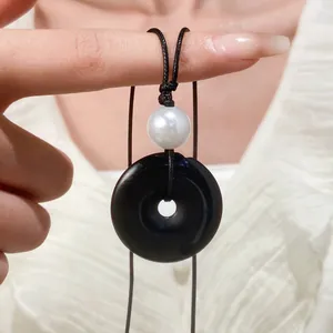Dettaglio della collana con pendente a cerchio nero con perla bianca e cordino