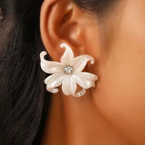 Detailed close-up of pearlescent lily flower stud earring with central rhinestone on ear