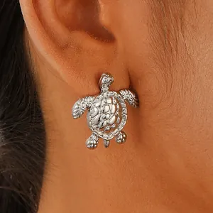 Close-up of a silver sea turtle stud earring worn on ear showing realistic textures
