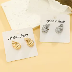 Detailed view of gold and silver conch shell stud earrings on white display card