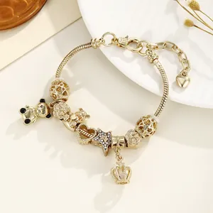 Détail du bracelet chaîne serpent dorée avec breloques cœur et couronne sur une assiette