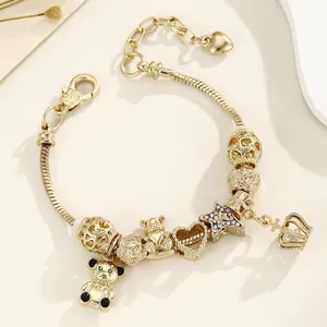 Détail d'un bracelet doré avec des breloques cœur, ours et couronne sur chaîne serpent