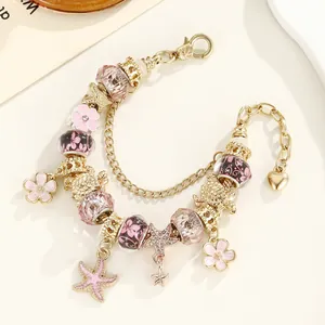Détail d'un bracelet à breloques dorées avec fleurs en émail rose et pendentif tortue de mer