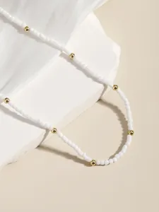 Detalle de collar de cuentas blancas y espaciadores dorados sobre tela de seda blanca