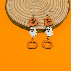 Detail of Halloween drop earrings with ghost and pumpkin elements on a wooden slice