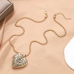 Détail du médaillon coeur vintage avec gravure florale et chaîne à billes sur soie