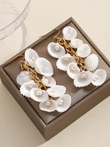 Detalle de pendientes largos con flores de concha blanca, perlas y borlas doradas