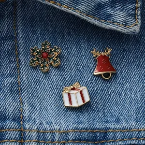 Three-piece Christmas brooch set with snowflake, bell, and gift box on denim fabric