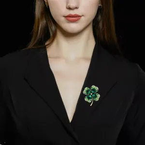 Détail d'une broche trèfle en cristal vert fixée sur un tissu noir portée par un mannequin
