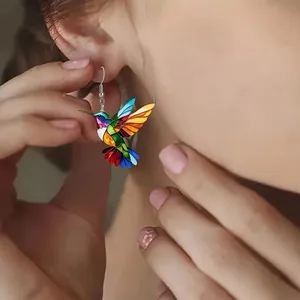 Close-up of a colorful hummingbird earring with enamel finish worn on a model ear