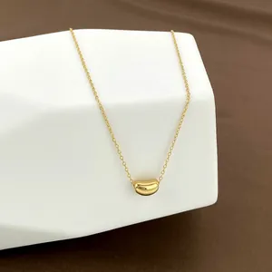 Minimalist gold bean pendant necklace in polished titanium steel on a white stand
