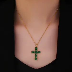 Close-up of golden cross necklace with green zircon stones worn over a black suit
