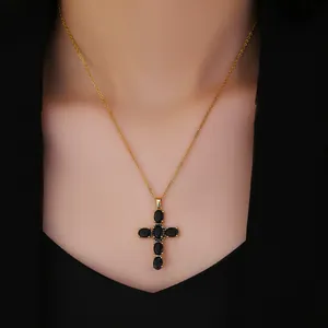 Detailed view of a gold cross necklace with black zircon stones on a model's neck