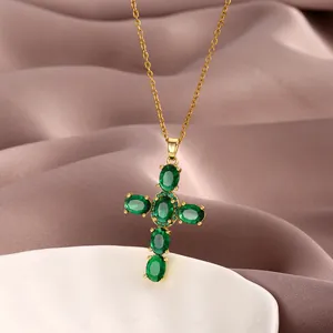 Detail of gold cross necklace featuring green zircon stones on silk fabric and ceramic plate