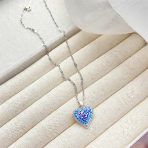 Detalle de un colgante de corazón plateado con cristais azules y cadena de eslabones
