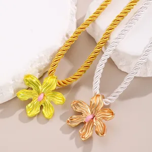 Macro view of metallic flower necklaces in yellow and rose gold with woven ropes