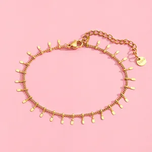 Close-up of golden stainless steel tassel bracelet with leaf charms on pink background