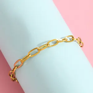 Detail shot of golden paperclip chain bracelet on a blue cylinder backdrop