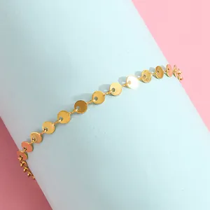 Detailed view of bohemian gold disc chain bracelet on a light blue cylindrical stand
