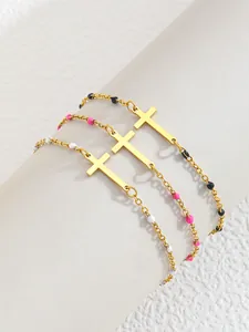 Detailansicht von drei goldenen Edelstahlarmbändern mit Kreuzanhängern und Emailleperlen