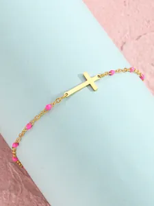 Detail eines goldenen Kreuz-Fußkettchens mit Kreuz und pinken Perlen auf blauem Zylinder