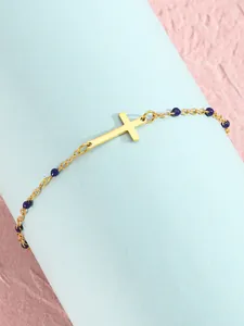 Detailansicht eines goldenen Kreuzarmbands mit dunkelblauen Perlen auf einem Ständer