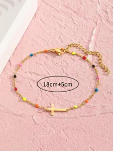 Detail der vergoldeten Edelstahl-Fußkette mit Kreuzanhänger und bunten Perlen auf Rosa Grund
