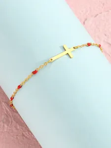 Nahaufnahme eines goldenen Kreuzarmbands mit roten Emaille-Perlen auf blauem Display