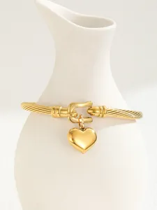 Detail of 18K gold-plated C-shaped cuff bracelet with twisted cable texture and heart charm
