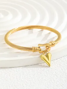 Macro shot of gold-plated twisted cable bangle with heart charm and buckle clasp details