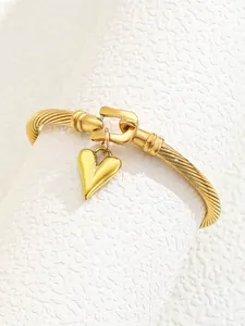 Close-up of a twisted gold cuff bracelet with a heart charm on a textured white stand