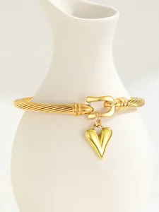Detail of twisted cable gold bracelet featuring a heart charm and U-shaped clasp