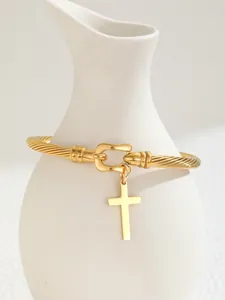Detail of 18K gold-plated C-shaped cable bracelet with horsebit buckle and cross pendant