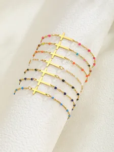 Détail de bracelets croix dorés avec perles colorées sur un support cylindrique blanc