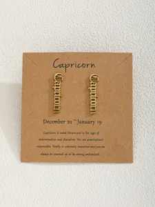 Détail de boucles d'oreilles signe Capricorne en métal doré sur support en papier kraft