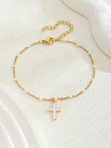 Détail d'un bracelet croix dorée avec perles en émail blanc et fermoir mousqueton