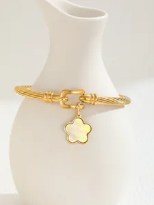 Detail of 18K gold-plated C-shaped cuff with shell flower pendant on a ceramic vase