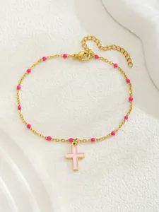 Détail d'un bracelet doré avec perles roses et croix en émail sur fond blanc épuré