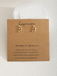 Dettaglio degli orecchini a perno Capricorno dorati con zirconi su cartoncino kraft