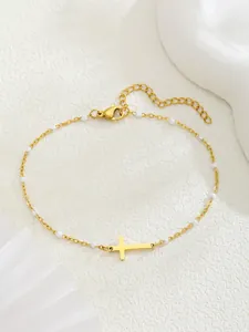 Détail d'un bracelet croix dorée avec perles blanches et fermoir ajustable sur fond blanc